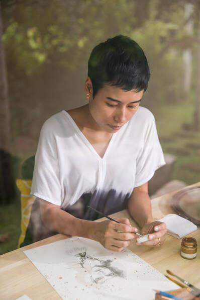 Adult Asian Female seated at studio desk painting |  Counseling for Artists, Online Creativity Counseling in Maryland and Virginia With Cindy Cisneros LCPC, LPC Creativity Coach, Counseling for Creatives and Highly Sensitive People HSPs