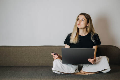 Picture of a woman sitting on a couch with a computer holding the credit card. Impulse shopping for creative personalities and neurodiverse individuals in Richmond, VA and beyond in the United States here.
