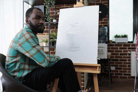 Picture of a black male artist looking lost with a blank canvas. Coaching for creative people in Baltimore, MD and online coaching for creatives in Maryland can help you find purpose here.  