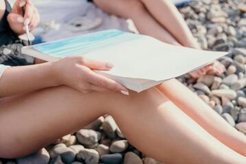 Picture of a woman's legs with a sketchbook as she draws a beach scene. Psychology for creative people, their needs and more can be found on this creativity coach's website. Learn about ADHD and creative people, neurodiversity, and more.