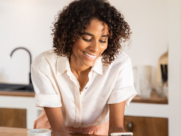 Black Female in kitchen using tablet, looking downward, smiling |  Creative People, Creative Minds, Creative Personalities, can find support with Creativity Coaching and Creativity Counseling at Creatively, LLC