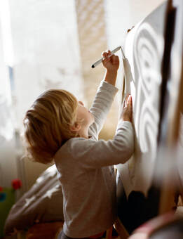 Caucasian child with blonde hair wearing white shirt painting on tall easel in classroom studio |  Creativity Counseling for Creative Children with ADHD With Cindy Cisneros, LCPC, LPC, Online Creativity Counseling in Maryland and Virginia