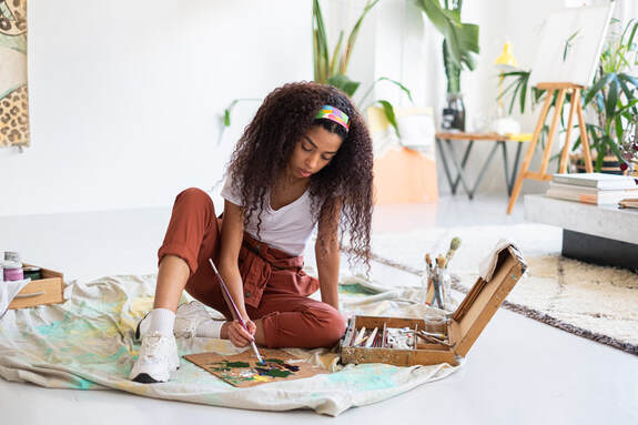 Black Young Adult Female painting in studio  on drop cloth over white floor |  Therapy for Creatives, Counseling for Anxiety and Depression and ADHD and Creativity, Counseling for Creatives in Maryland and Virginia, Therapy for Creatives With Cindy Cisneros, LCPC, LPC