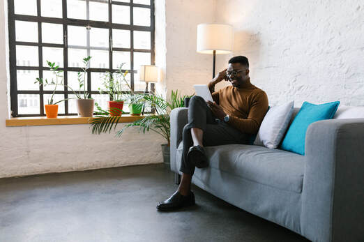 Black Man seated on gray couch with laptop | Online Coaching for Creative People at Creatively, LLC