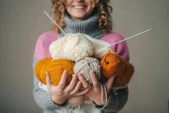 Picture of a woman holding balls of yarn and knitting needles out to the camera. Get started with creativity coaching in Richmond, VA and Baltimore, MD and the Washington D.C. area here! A creativity coach in the United States, Canada, Germany, UK and beyond can help!