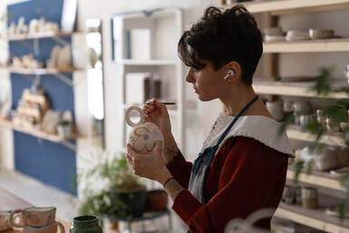 Picture of a woman doing art, pottery and listening to courses and creativity studio work in her air pods. Get started with creativity coaching in Richmond, VA and Baltimore, MD and the Washington D.C. area here!
