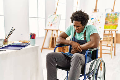 Picture of a black male artist in a wheelchair holding his stomach and looking like he is in pain. Creative people in Maryland and Virginia can get help with a creativity coach based in Richmond, VA or creativity counseling near Baltimore, MD here. 