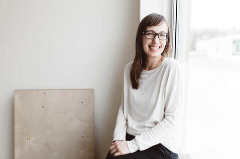 Caucasian Adult Female in glasses in studio with white walls seated at window in daytime, smiling |  Creative Therapy, Counseling for Artists With Cindy Cisneros, Counseling for Creative People in Maryland and Virginia 
