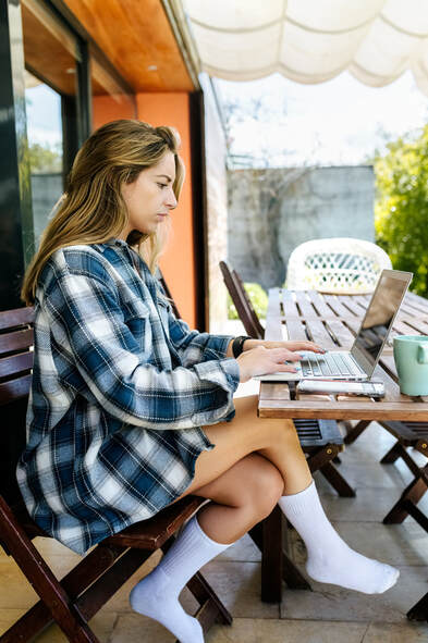 Young adult, Caucasian, in plaid shirt sitting in outdoor cafe, using laptop |  Coaching for Creative People is flexible, use anywhere, anytime, with shorter sessions and asynchronous support