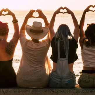 Picture of women holding heart hands in the air on the beach. Therapy for artists in Virginia and Maryland can help you find grounding through mindfulness practice in Richmond, Baltimore and beyond.